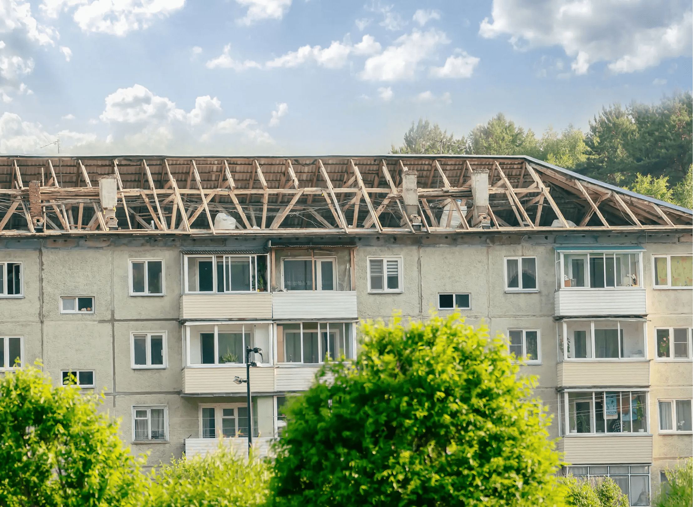 Building with damaged roof and green trees.